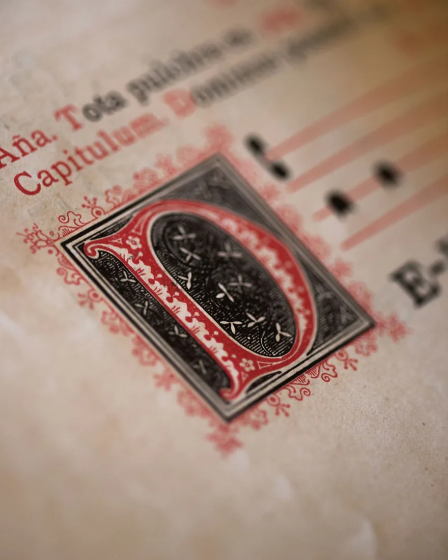 Zdobená iniciála ve starém rukopisu s barevnou ornamentikou a psaným textem